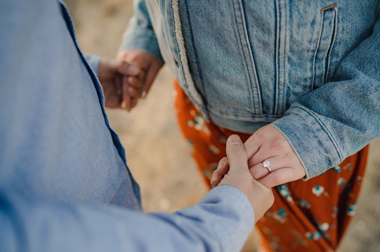 A couple holding hands, the woman wearing a solitaire engagement ring.