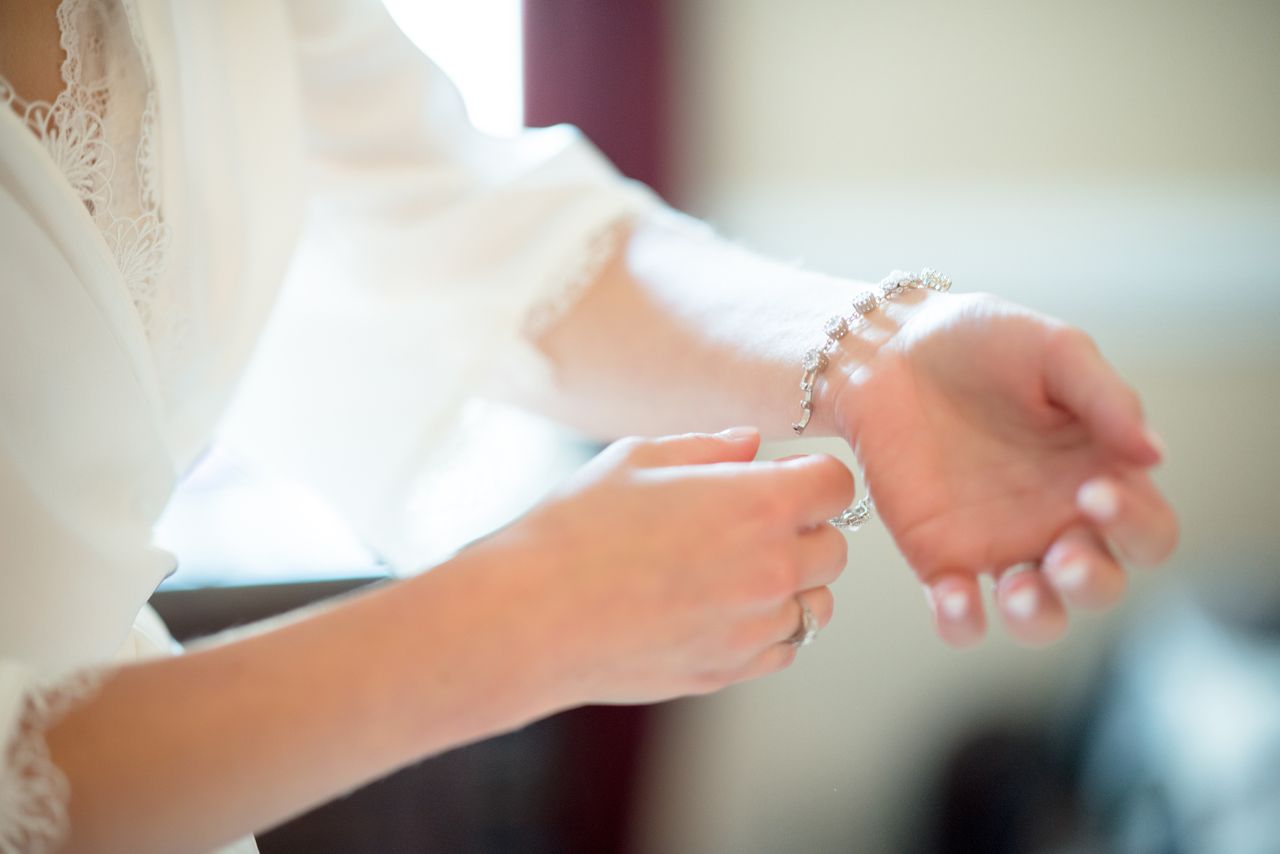 A woman in a lacy white robe puts on a diamond bracelet.