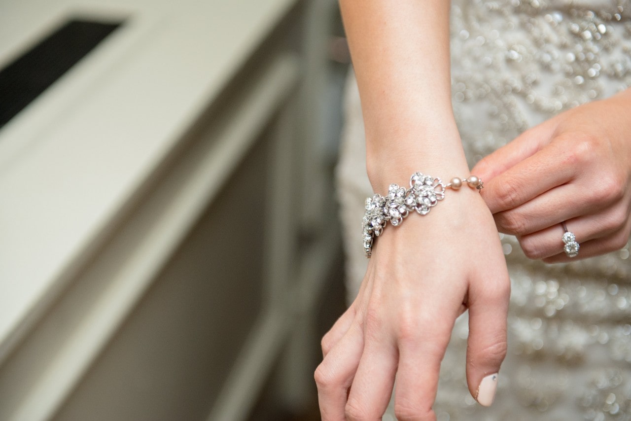 A woman in a sparkly formal gown adjusts her pearl and diamond bracelet.