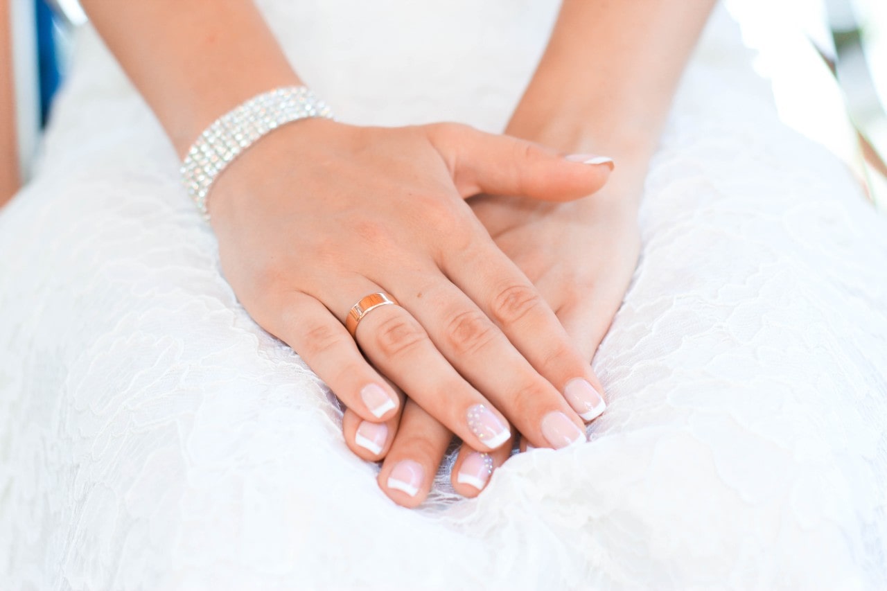 A bride wears an elaborate diamond bracelet while resting her hands in her lap.