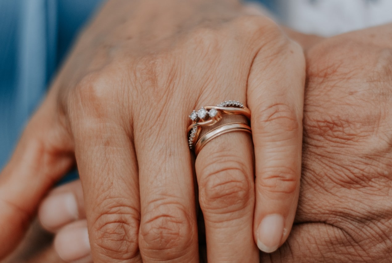 close up image of an older couple’s hands, one of which is wearing two gold rings