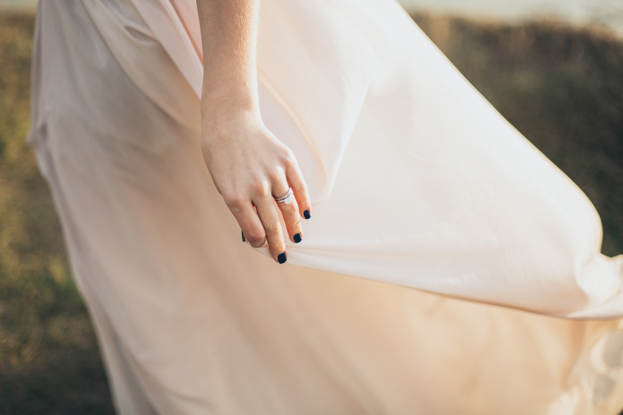 A close-up of a bride’s hand as she grabs her dress, wearing her bridal jewelry.