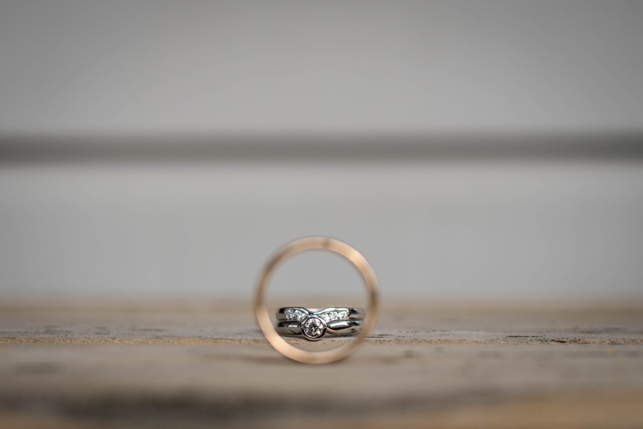 An engagement ring and a wedding band viewed through a gold men’s wedding band.
