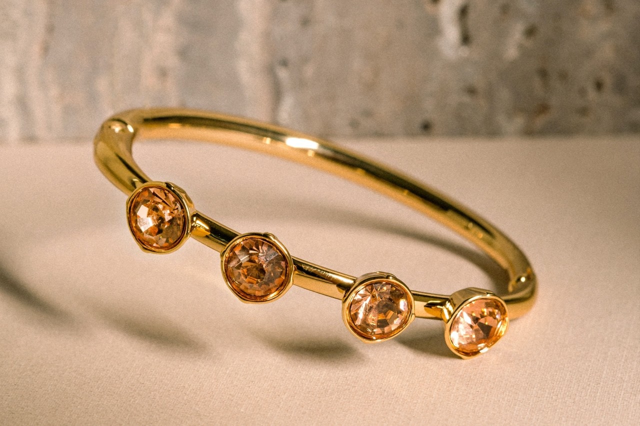 a yellow gold fashion ring featuring four orange gems on a tan surface