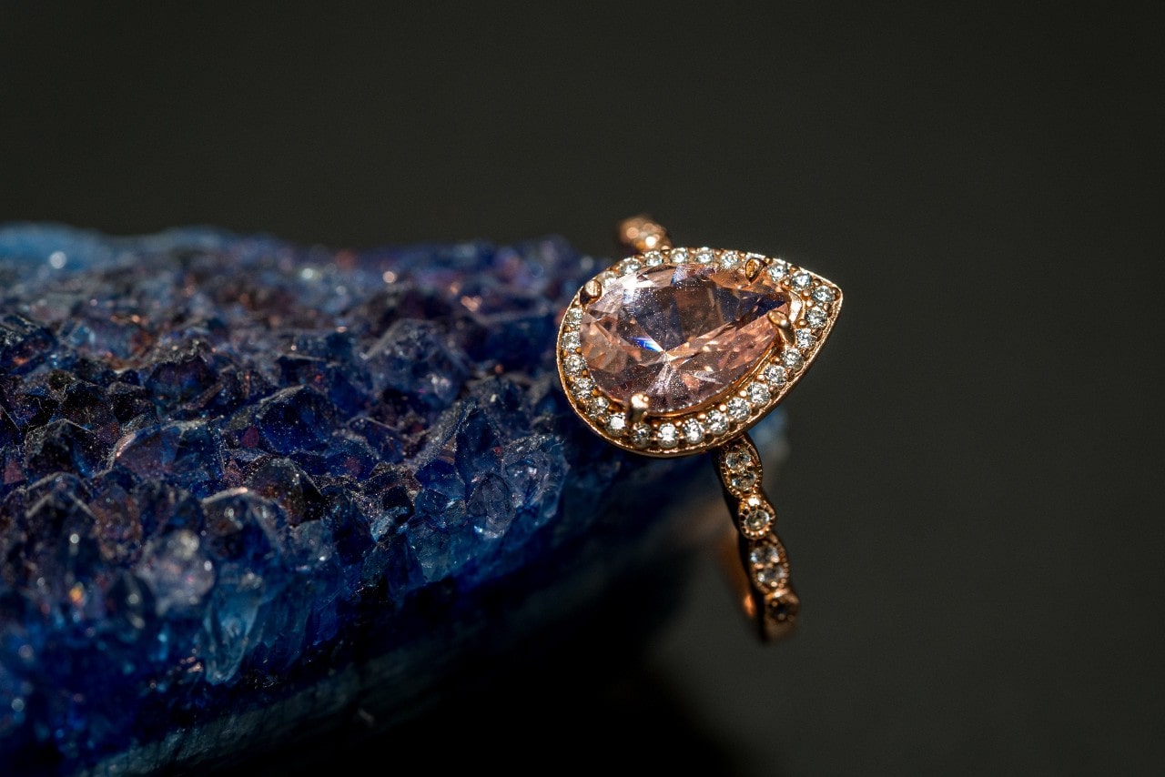 a gold gemstone ring featuring a pear shape, orange gem, resting on a large blue stone