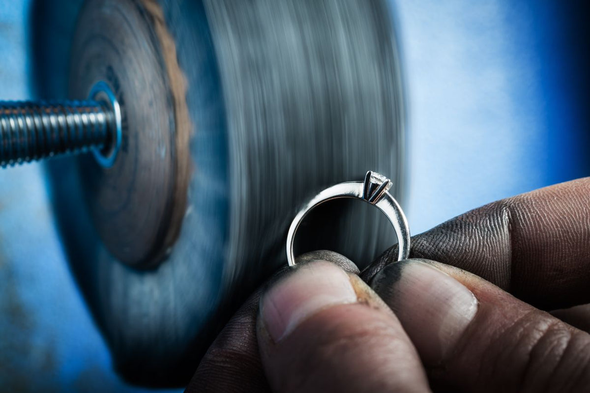 A jeweler with dirty hands polishes a solitaire engagement ring at his workstation