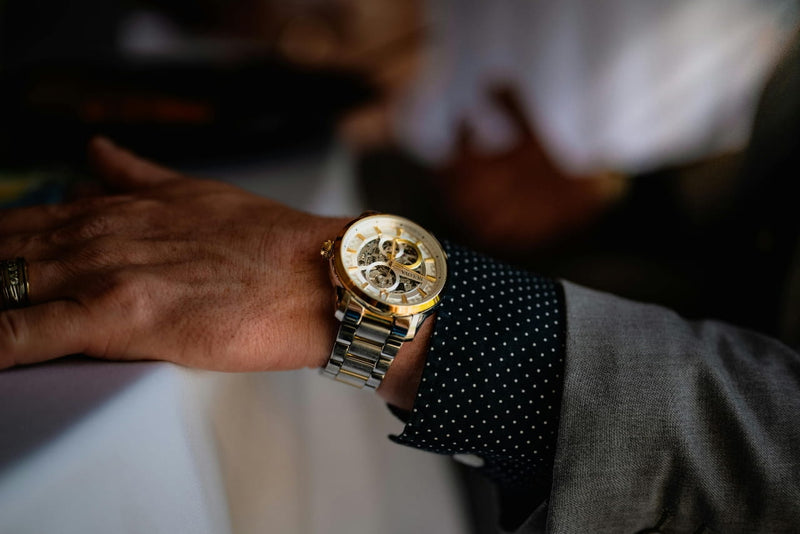 Close-up of a man's wrist wearing a gold and silver Bulova skeleton watch with a grey suit.