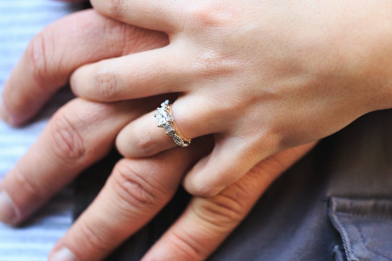 a couple holding hands, the woman wearing a mixed metal, three stone engagement ring