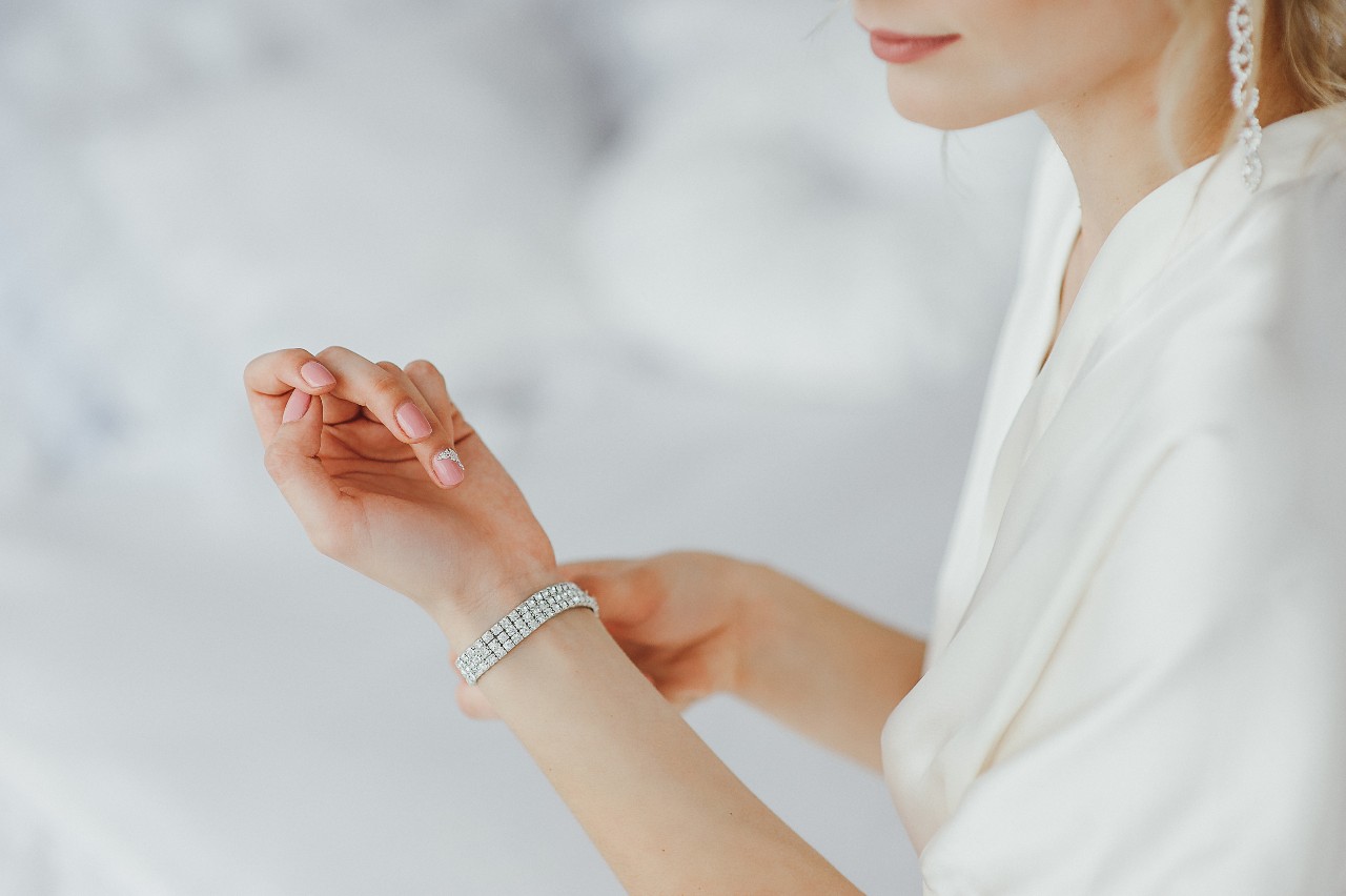 A woman in a white robe clasping a sparkling diamond bracelet on her wrist.