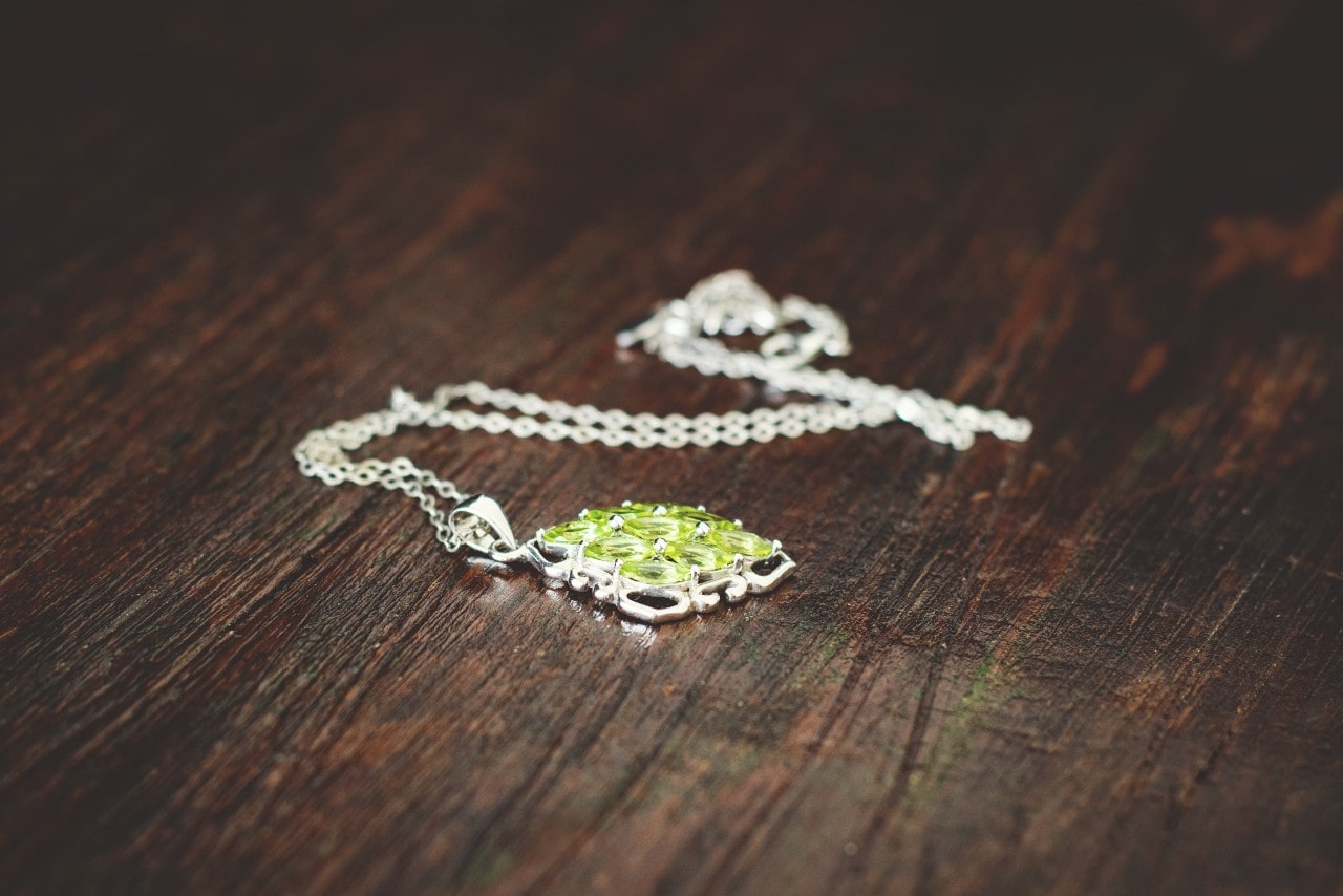 A chain necklace with a bright green oval pendant rests on a dark wooden surface.