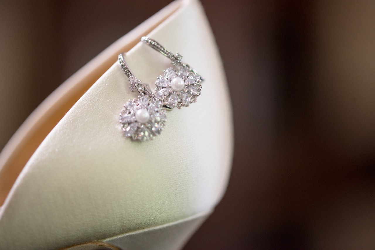 Elegant pearl and diamond earrings rest on a creamy satin high heel.