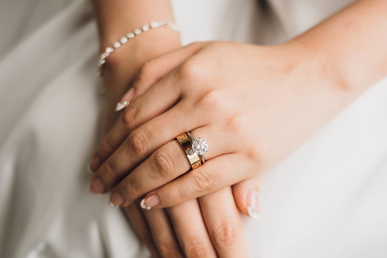 A close up of the bride's manicured hands with a solitaire diamond engagement ring and wedding band.