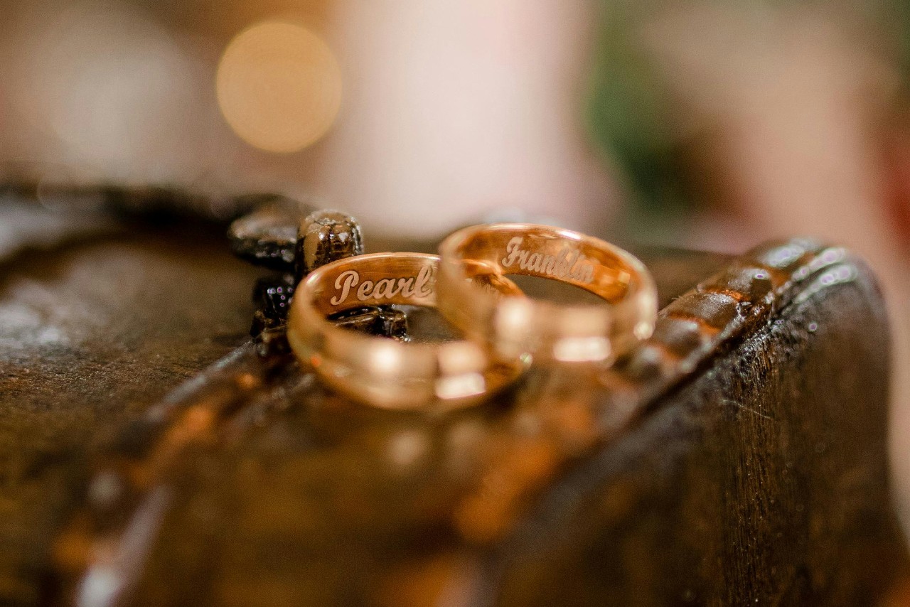 Two yellow gold wedding bands resting on rustic wooden surface with engraved names on the inner side.