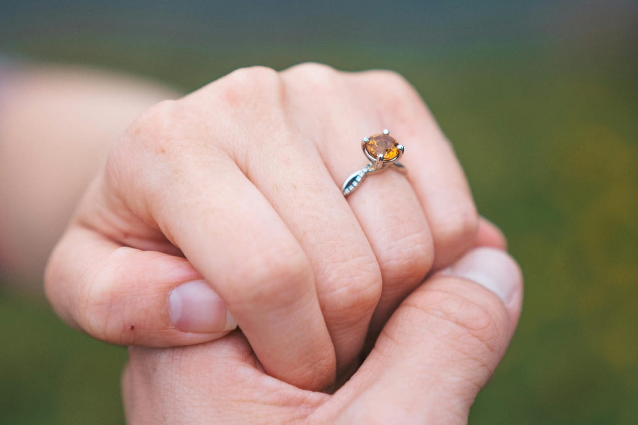 A close up of a hand, adorned with an intertwined white gold engagement ring with a citrine centerpiece.