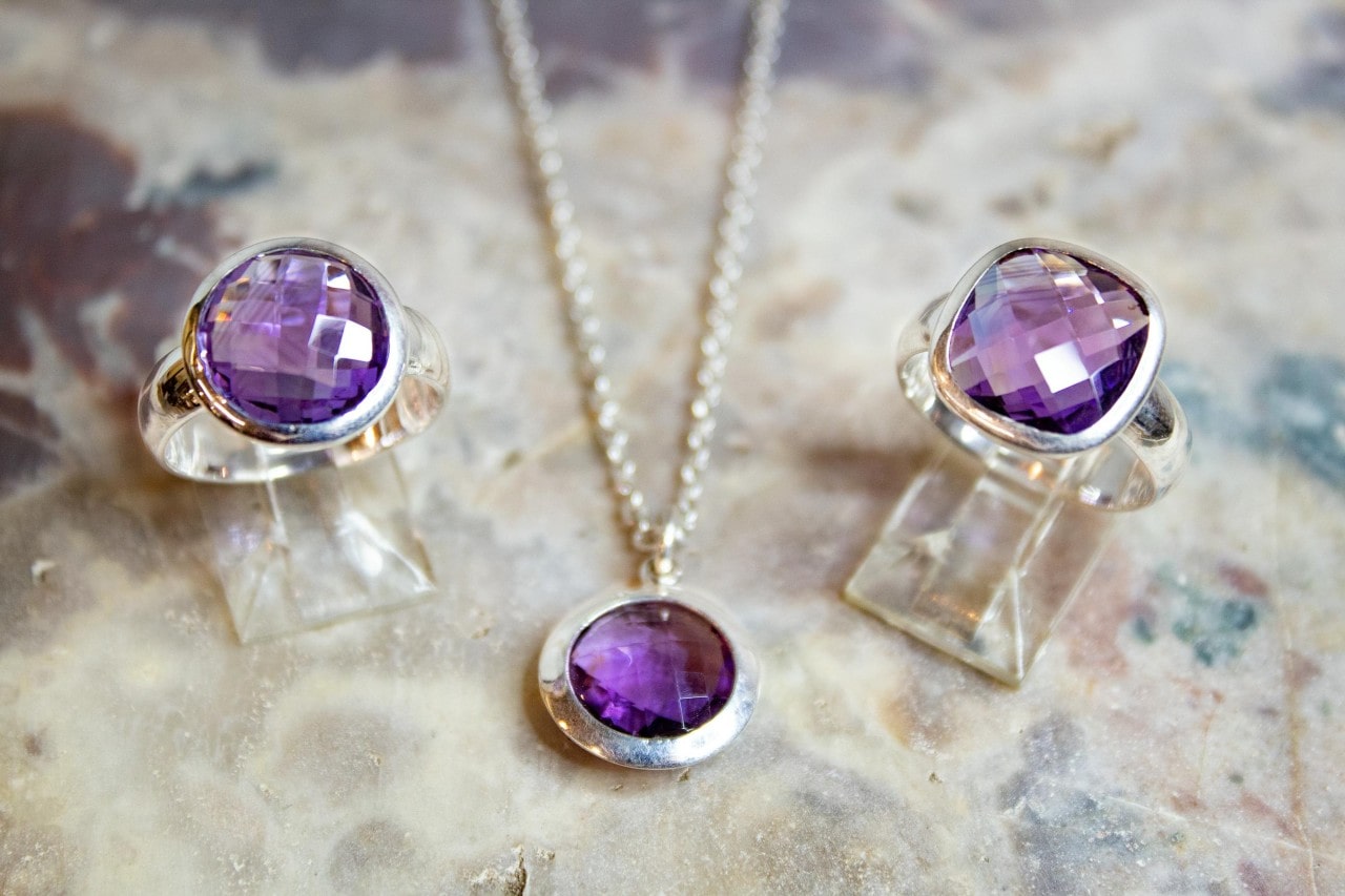 A set of white gold jewelry, featuring bezel set amethyst round pendant, and two fashion ring on a marble surface