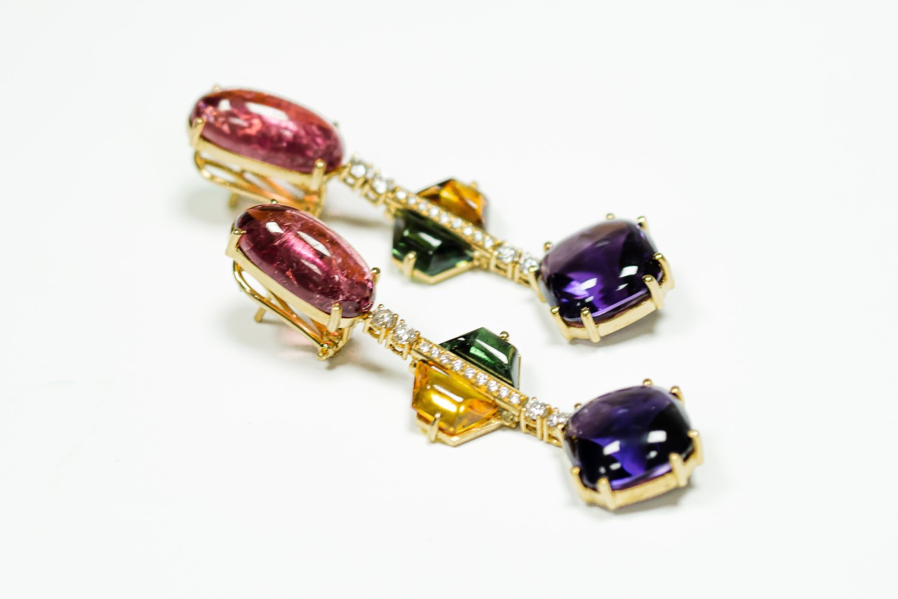 A close up of gemstone earrings, featuring red, green, yellow and purple crystals