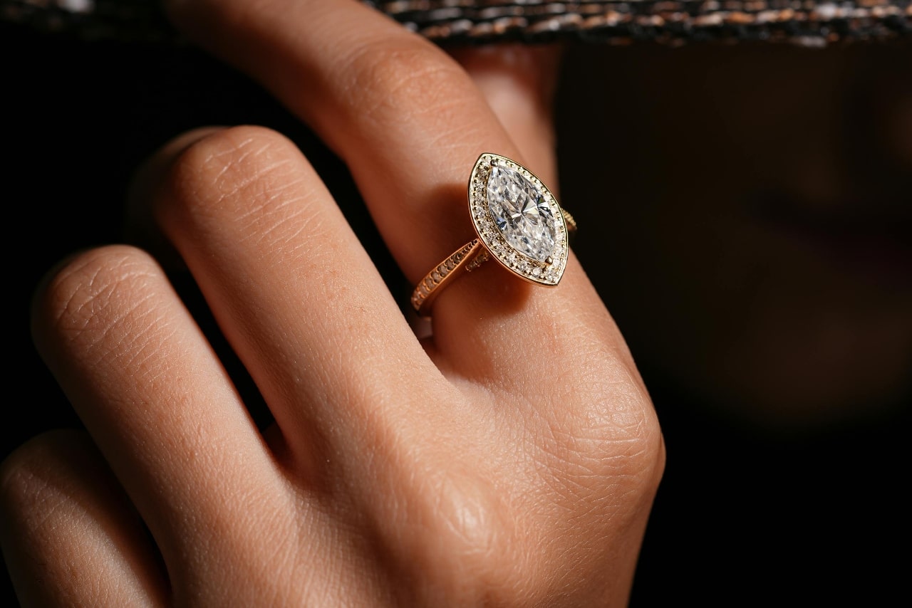 A close-up of a marquise cut engagement ring with a diamond studded bezel and band.