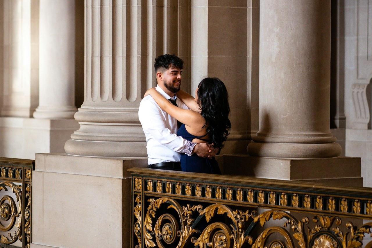 A nicely dressed couple dancing on an intricate balcony surrounded by large pillars.