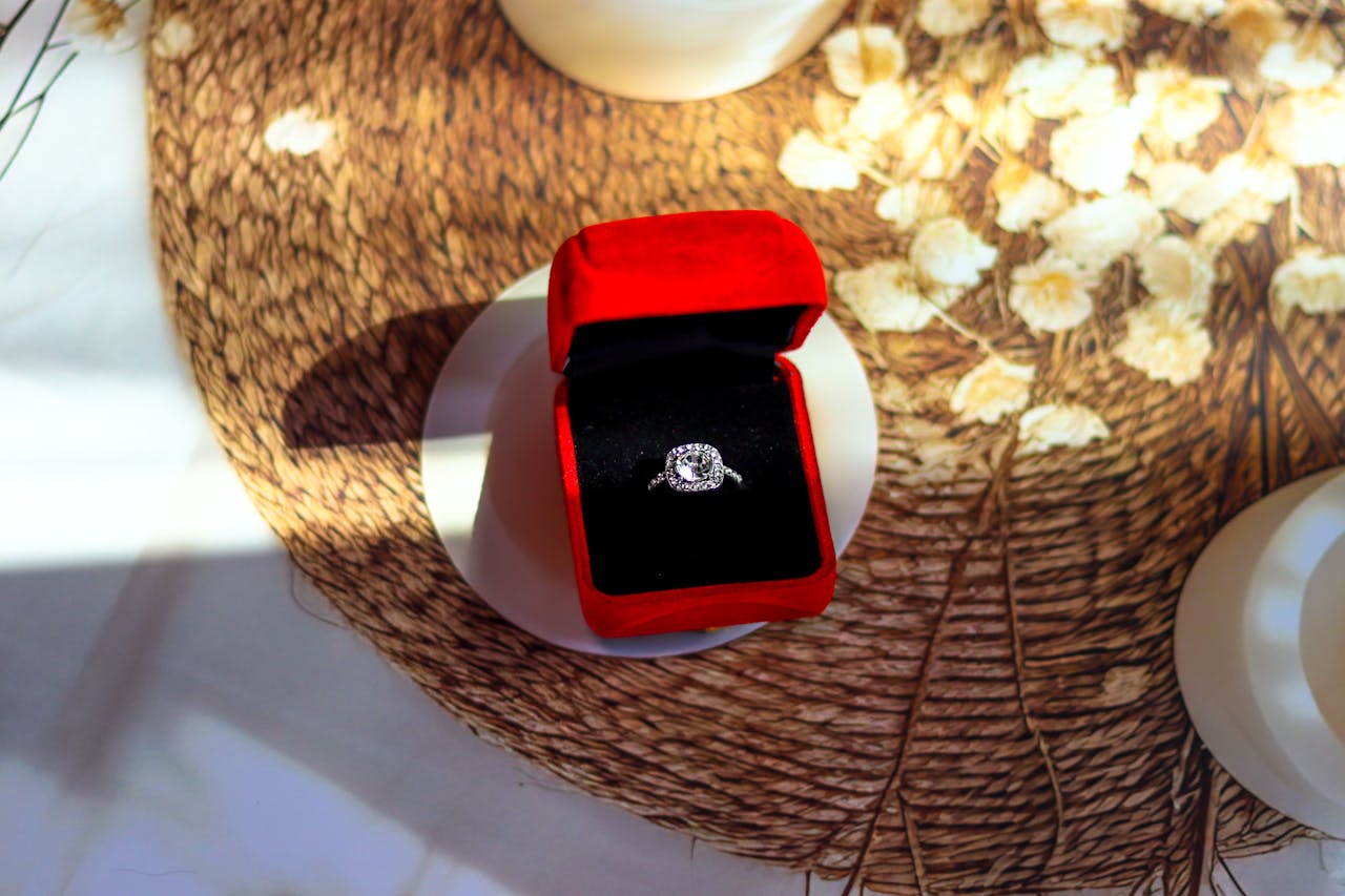 A white gold halo diamond engagement ring inside the red velvet jewelry box on top of the tupperware