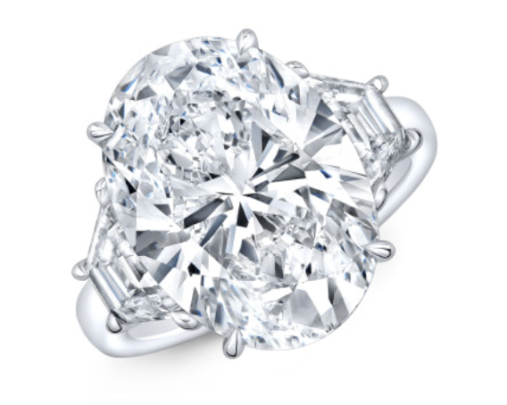 A platinum three stone diamond engagement ring with oval center stone and emerald side stones