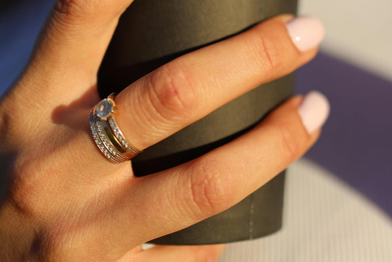 A close-up of a person’s hand adorned with a stacked wedding band and an oval engagement ring holding a coffee cup.