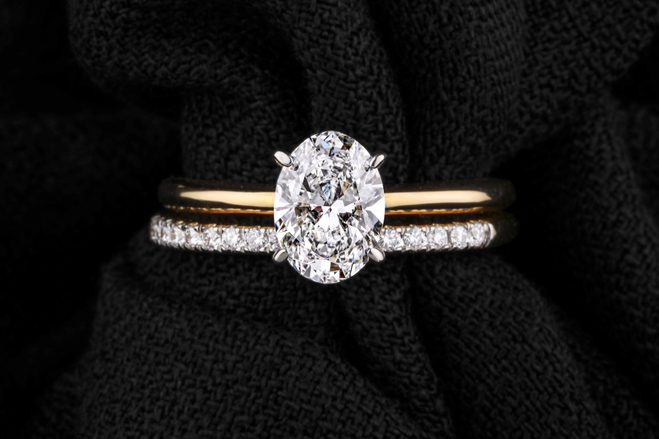 An oval cut engagement ring stacked with a diamond pavé wedding band against a black fabric background.