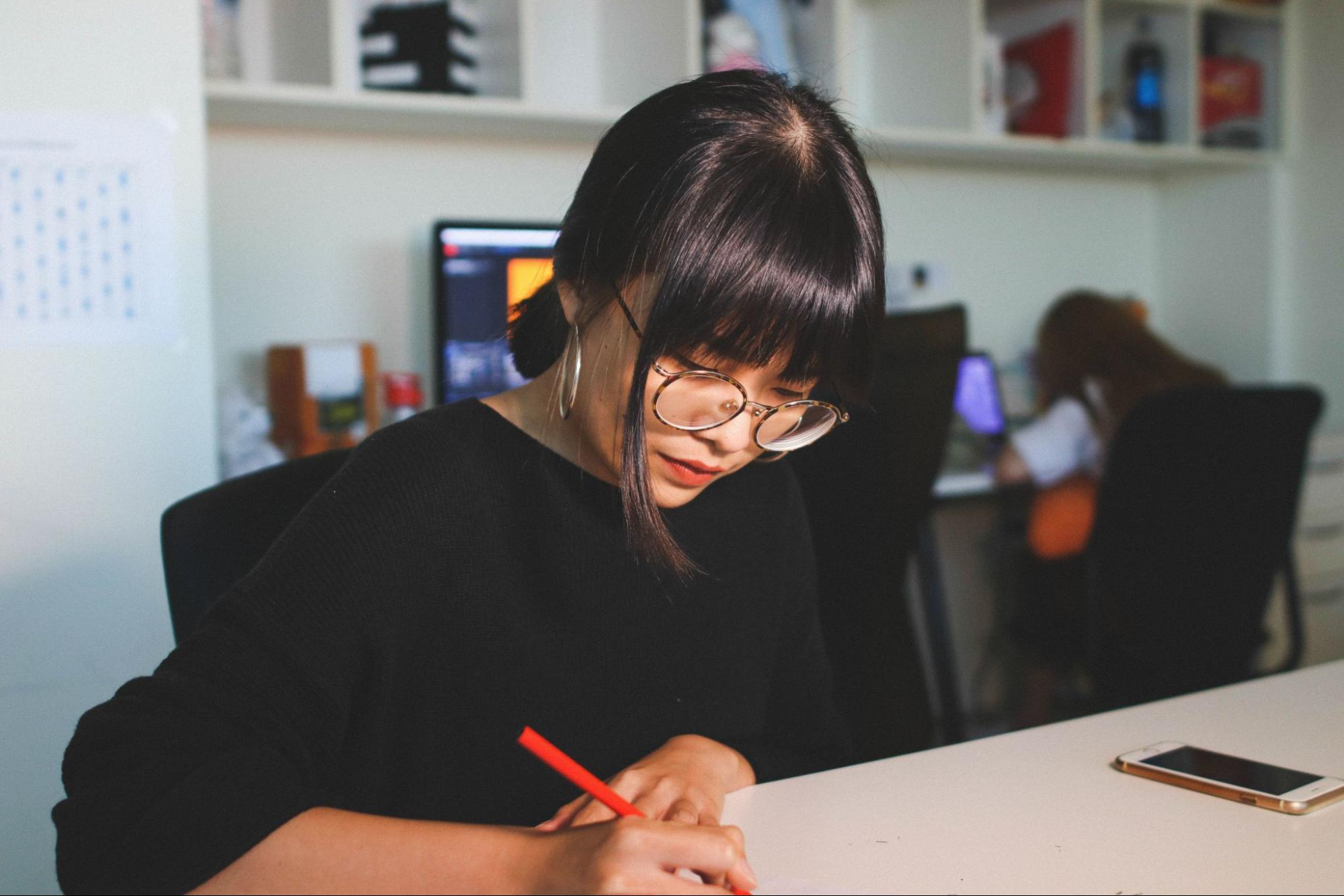 An artist sketches an idea on a piece of paper while wearing white gold hoop earrings.