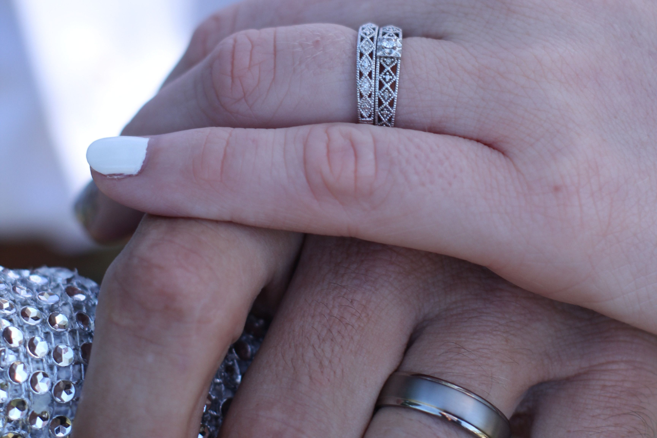 A woman resting her hand on top of a man’s, she has two gorgeous engagement rings on and her partner has a silver wedding band.
