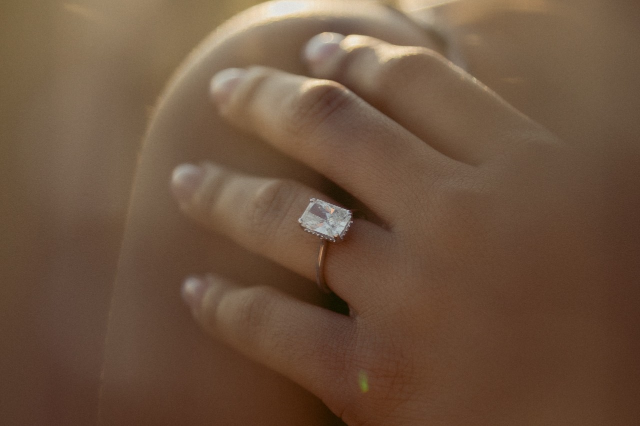 a woman’s hand resting on her shoulder and adorned with a radiant cut engagement ring