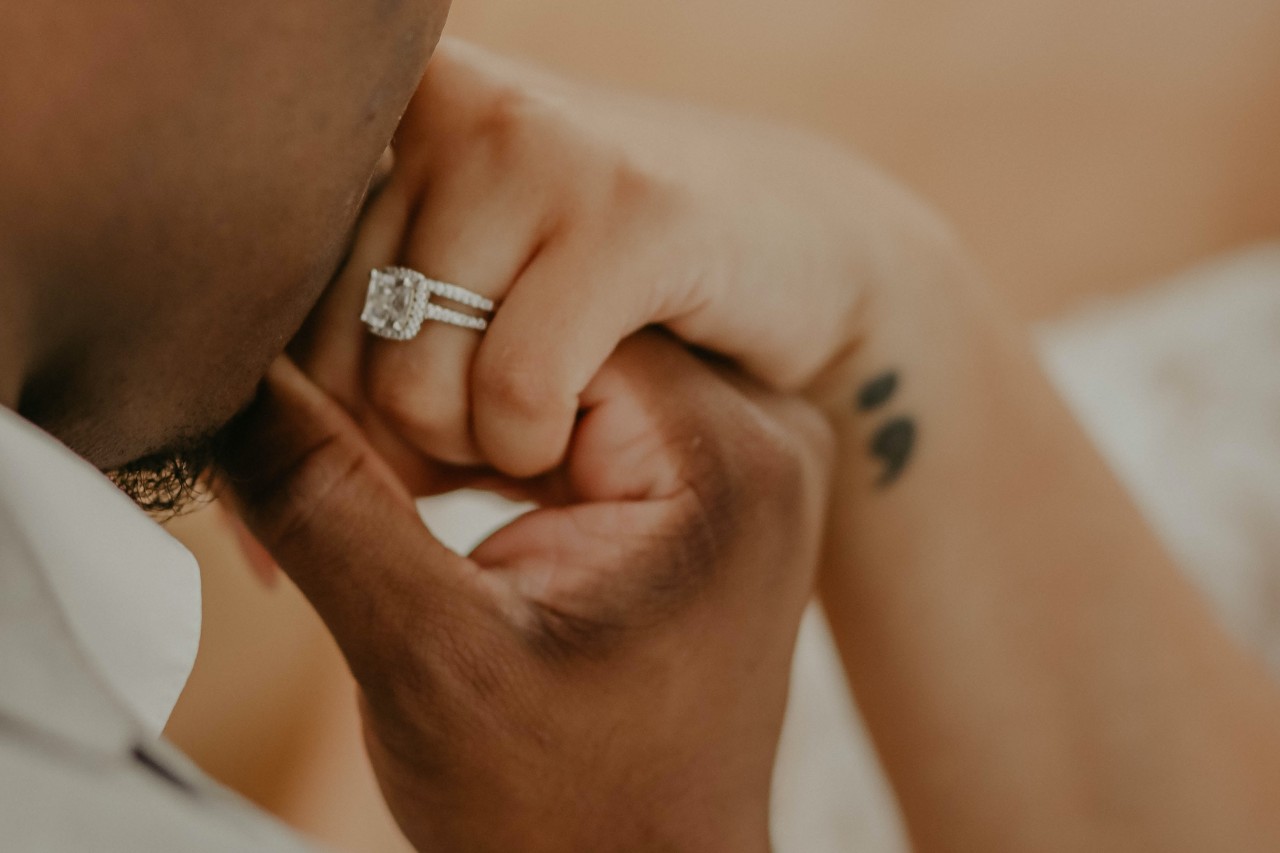 a groom kissing his bride’s hand, his bride wearing a radiant cut engagement ring