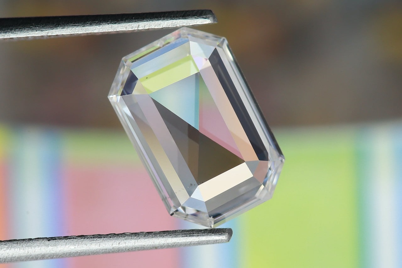 an emerald cut diamond held up by a pair of silver tweezers