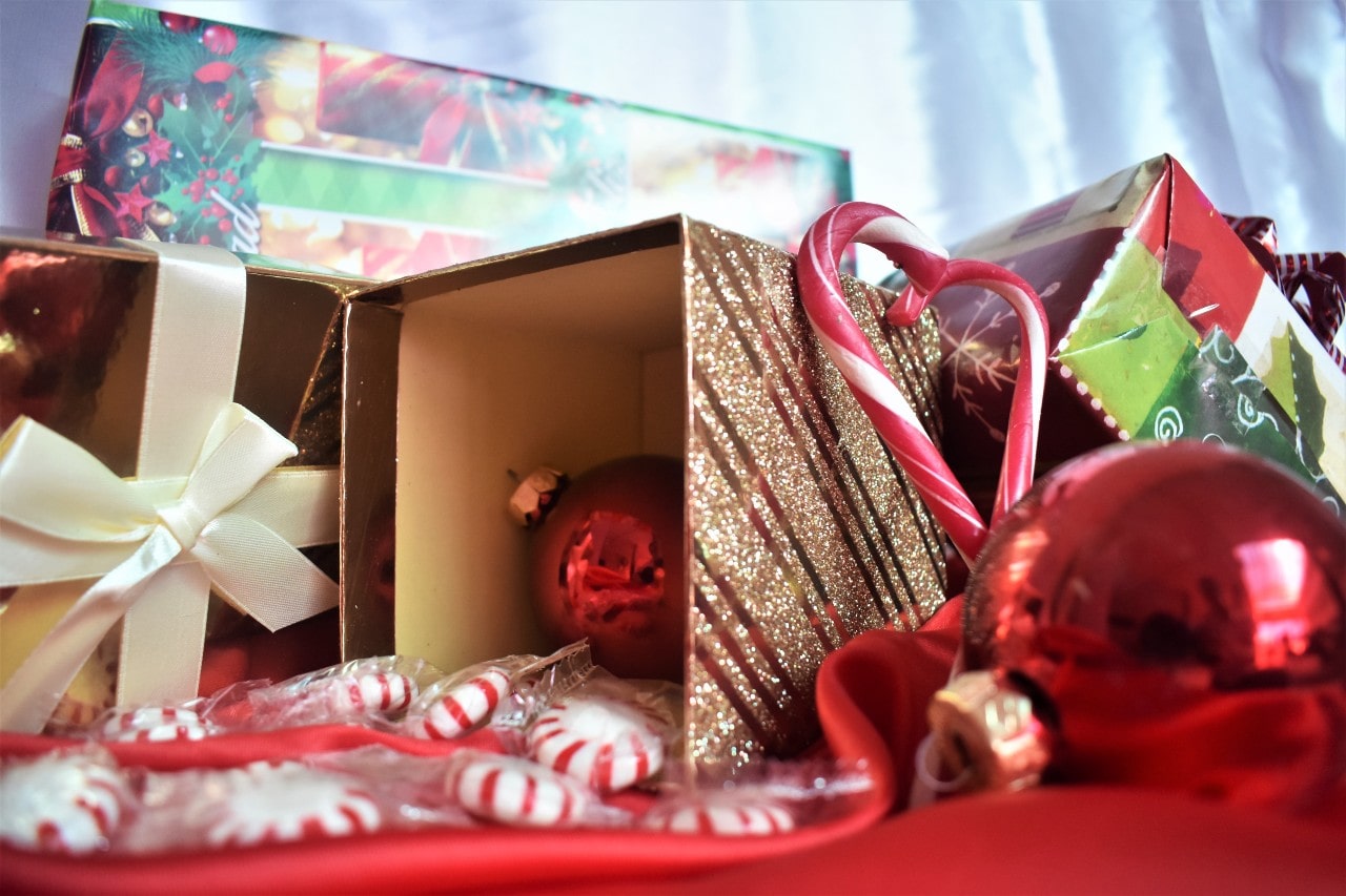 A close-up of several festive Christmas gift boxes with round red Christmas toys and candies.