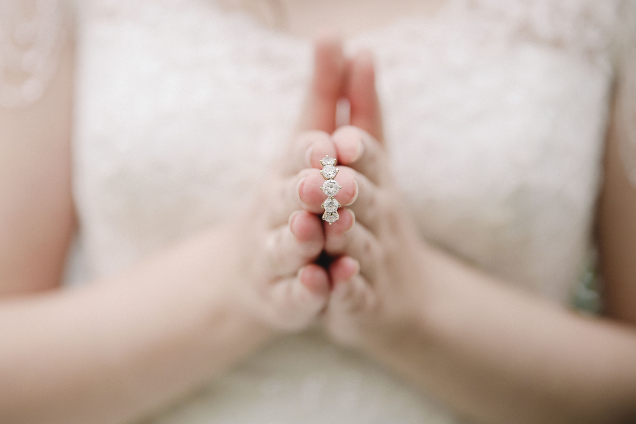A close-up of a bride holding a 5 stone diamond engagement ring between her fingers.