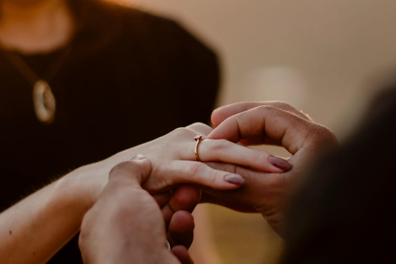 A close-up of a person putting a rose gold diamond engagement ring on another person’s hand.