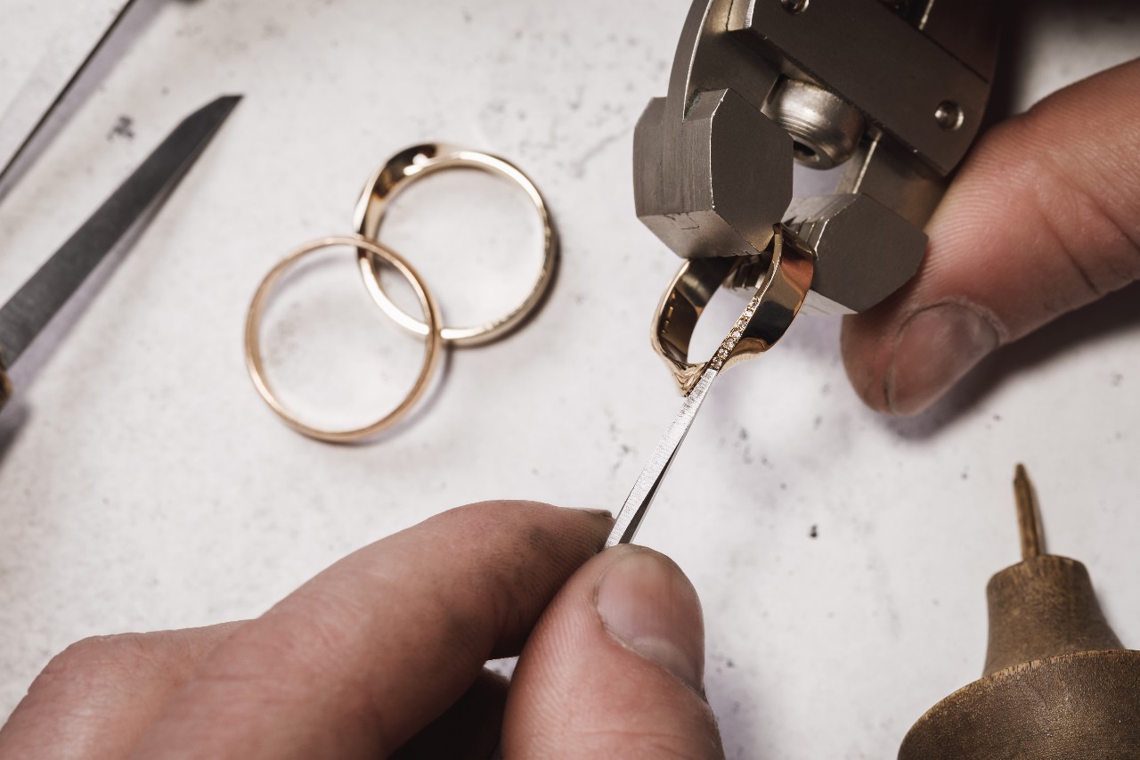 A close up of jeweler modifying yellow gold wedding bands with tweezers and specialized tools.