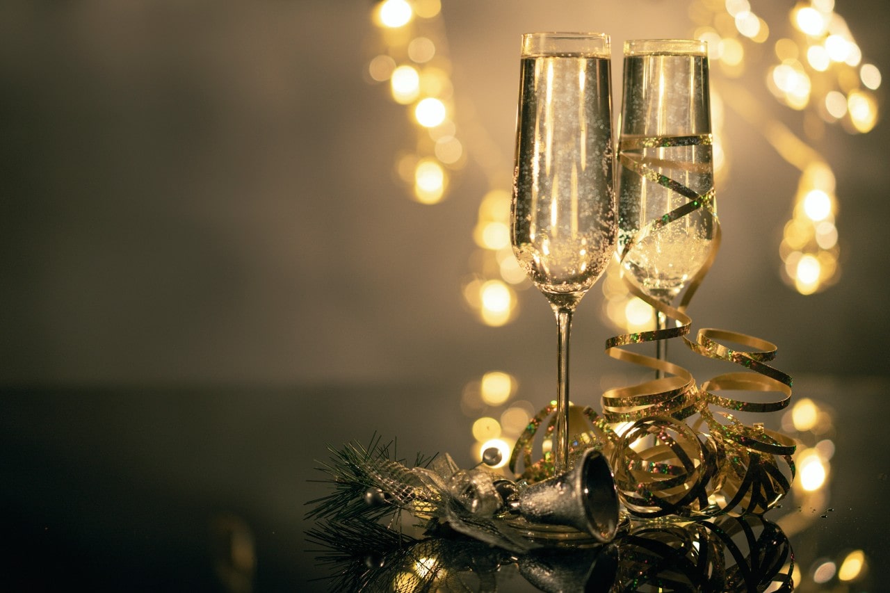 two champagne flute glasses sit by gold ribbon and New Year’s decorations.