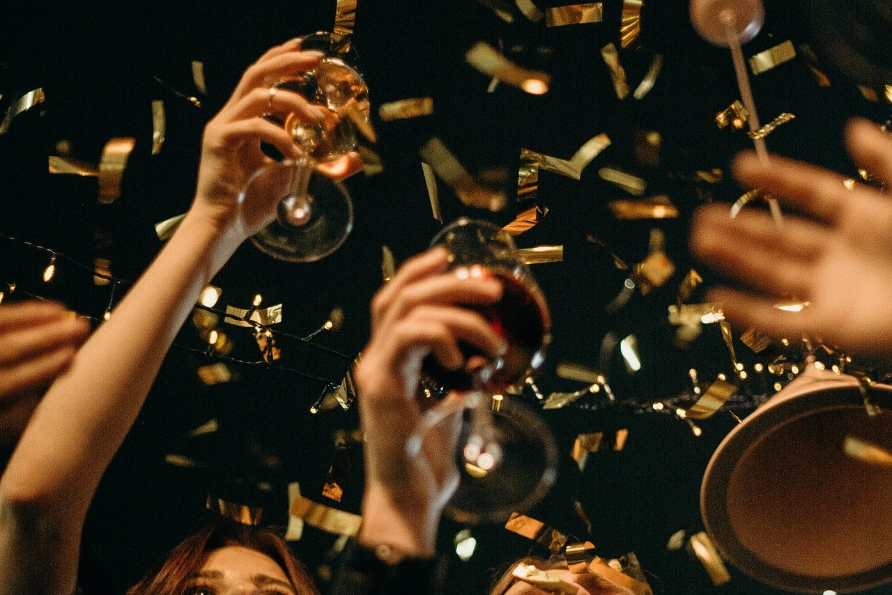 A group of friends raise their wine glasses as gold confetti falls.