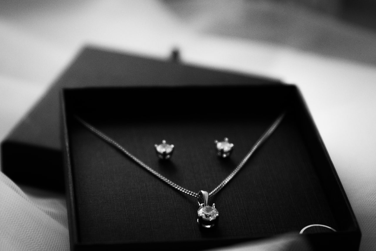 Elegant jewelry set showcasing a sparkling diamond pendant on a fine chain with coordinating earrings, artfully arranged on a dark velvet box.