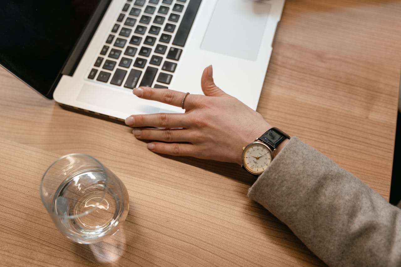 A woman working on her laptop atop a wooden desk, with emphasis on the luxury watch on her wrist.