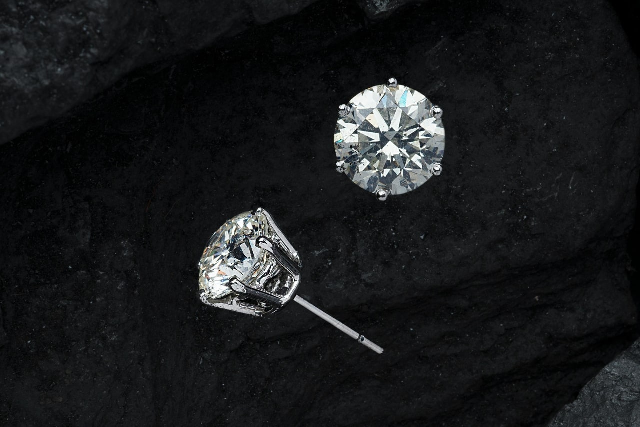 A close-up of a pair of diamond earring studs on a black felt background.