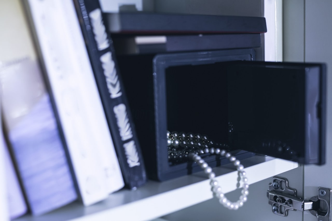 A close-up image of an open jewelry safe on a shelf with a string of pearls hanging slightly out of it.