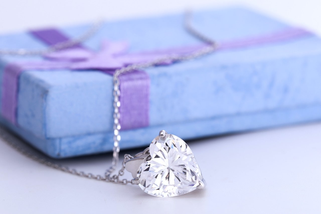 a heart diamond necklace sits by a blue gift box with purple ribbon.