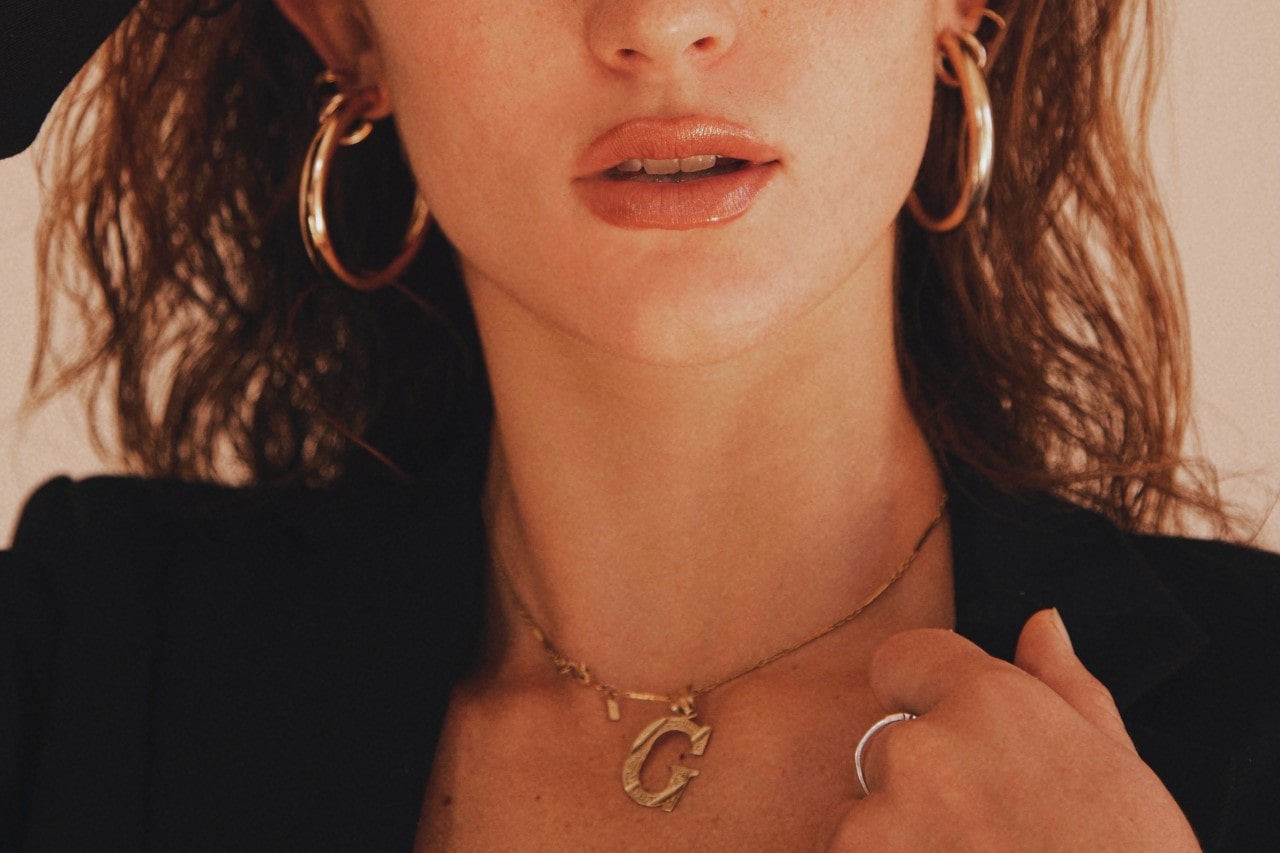 A woman wearing a “G” pendant with gold hoop earrings and a ring.