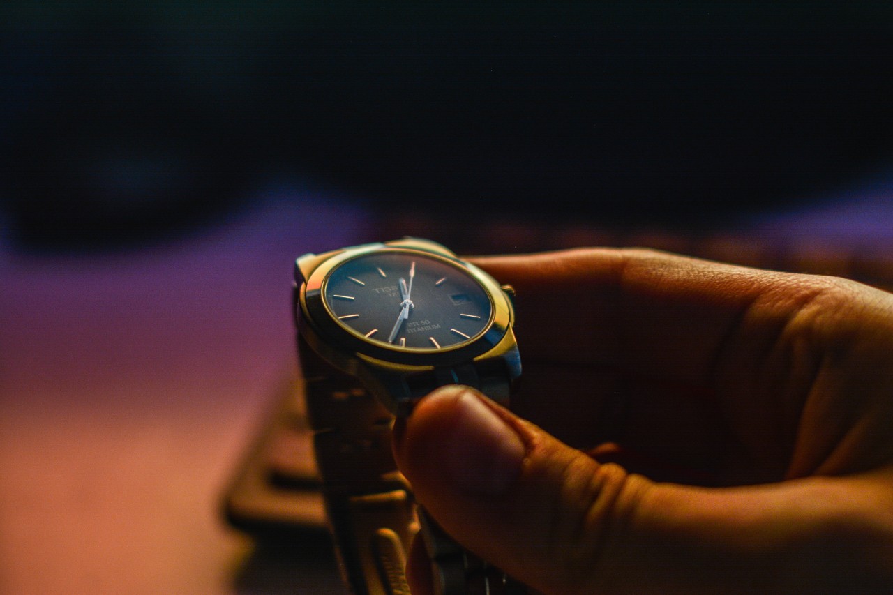 Closeup of a metallic watch in man’s hand against a blurred warm lit background.