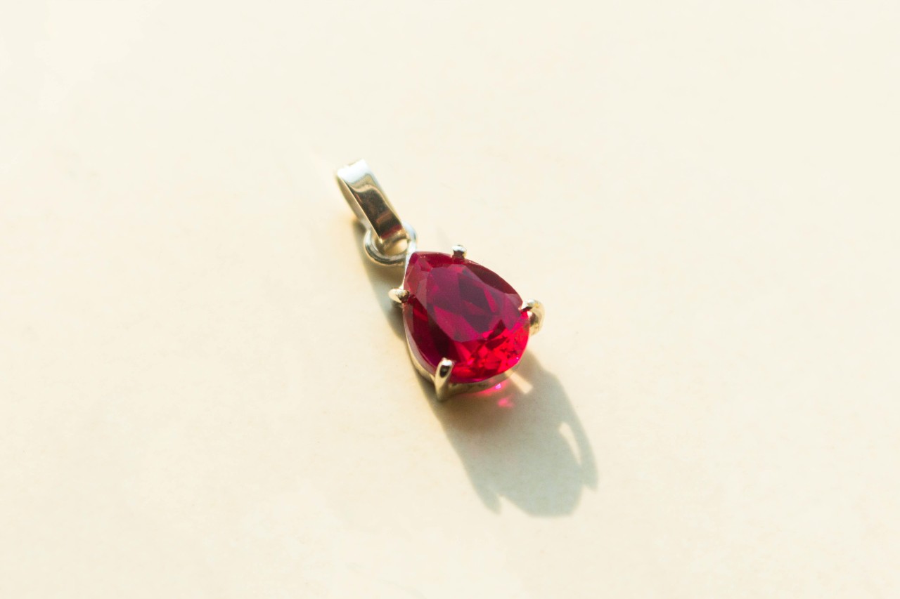 A close up of a teardrop-shaped ruby pendant set in silver on a light background.
