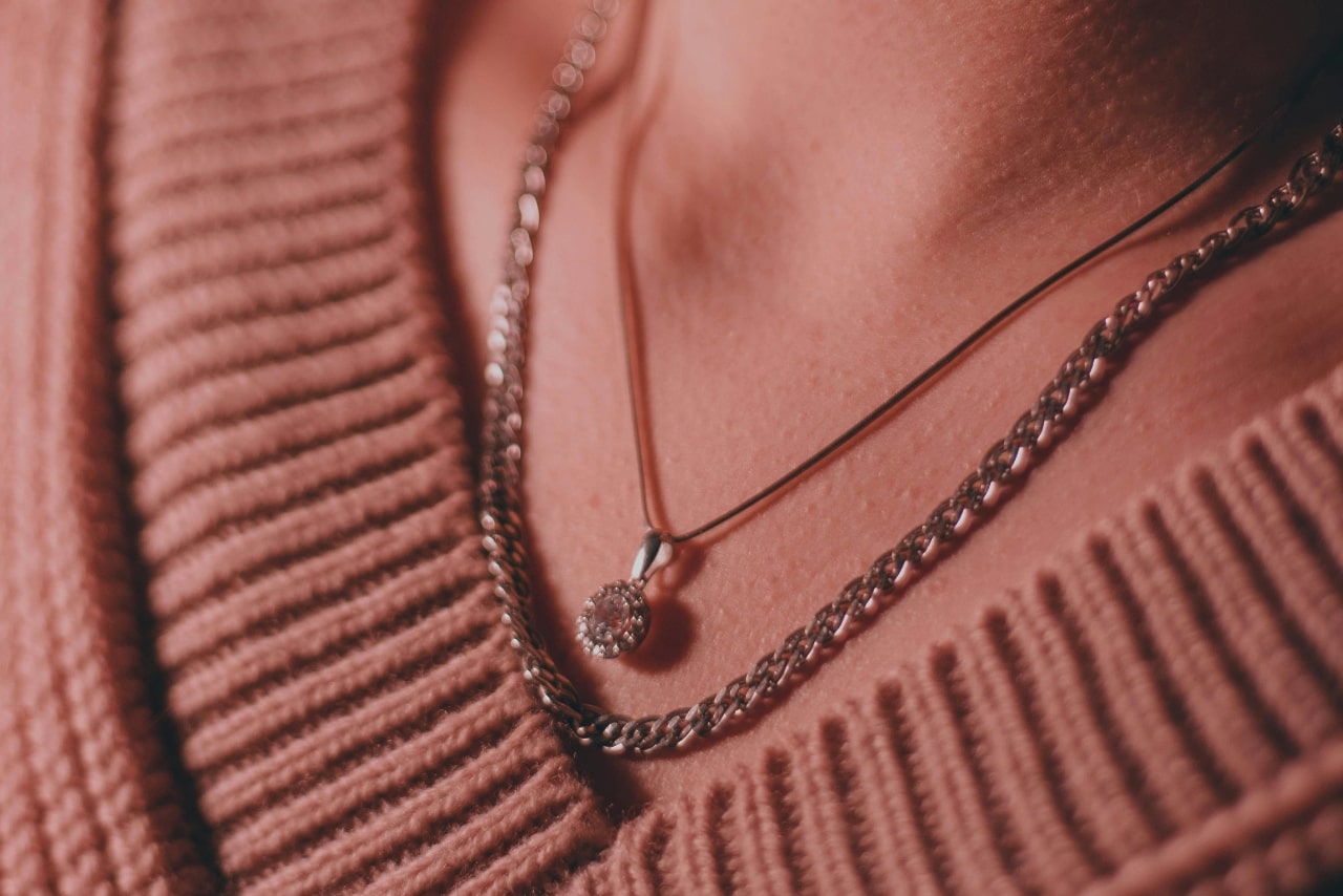 A close-up of a person wearing a halo diamond pendant necklace layered with a thicker chain over a ribbed sweater