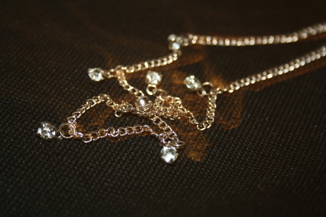 A delicate gold chain with small clear crystals is artfully arranged on a dark textured surface.