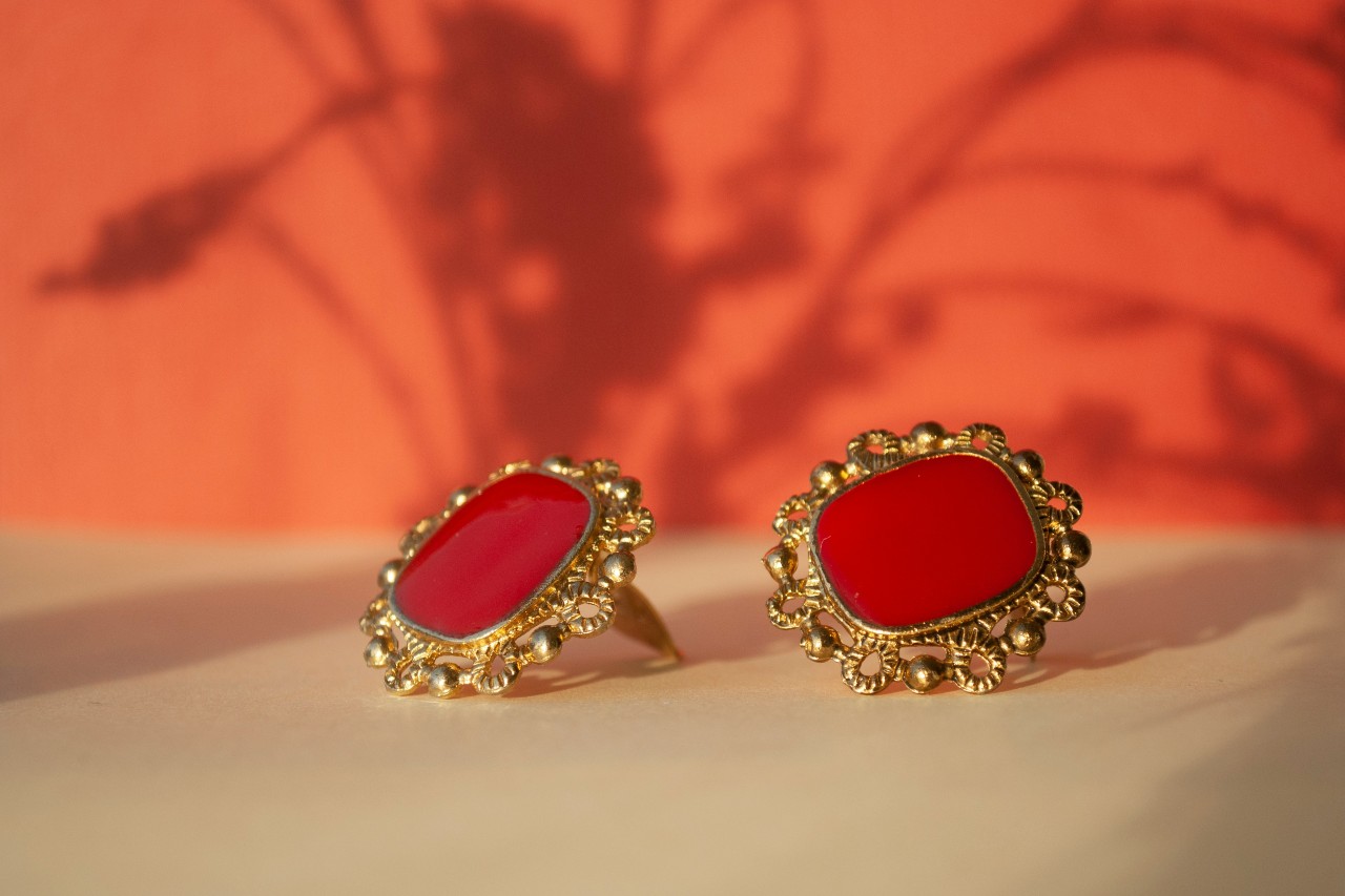 Red stone earrings with ornate gold settings against a warm orange background.
