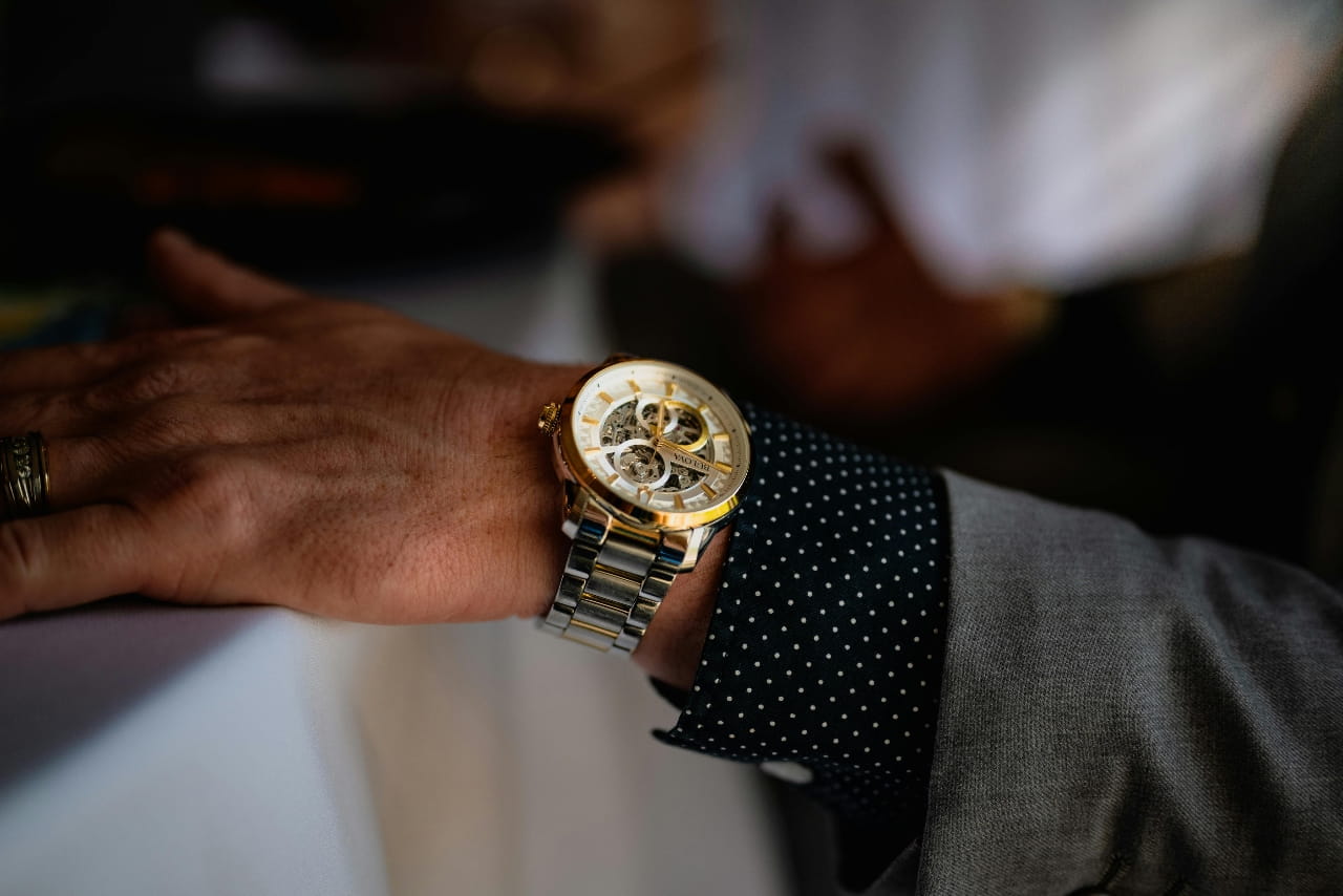 Close-up of a man's wrist wearing a gold and silver Bulova skeleton watch with a grey suit.