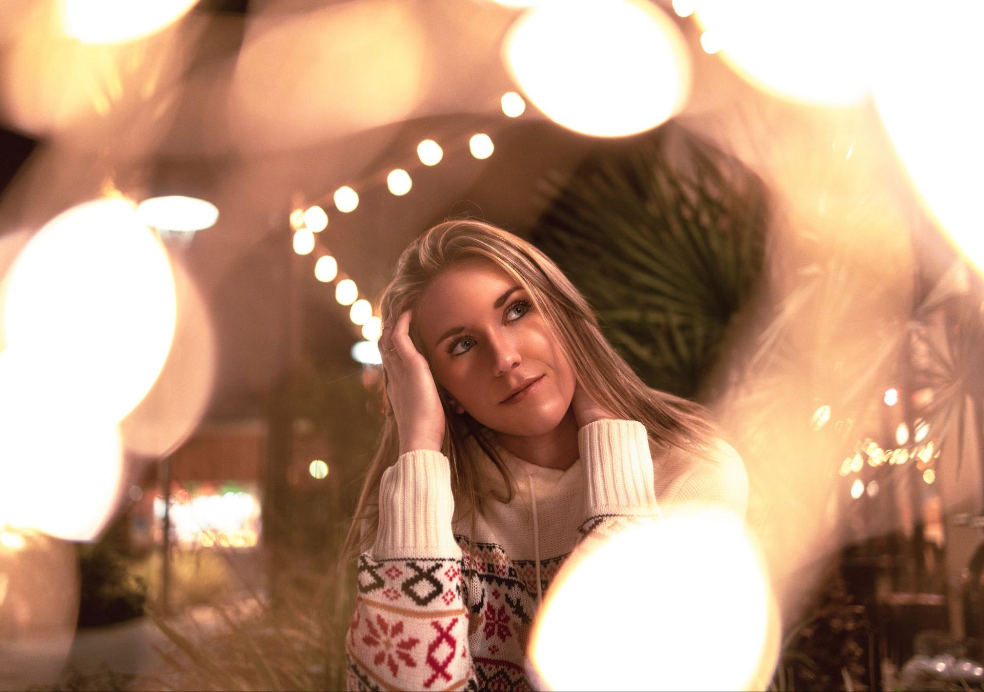 A woman in a knitted sweater sits and looks away in a bokeh lithing